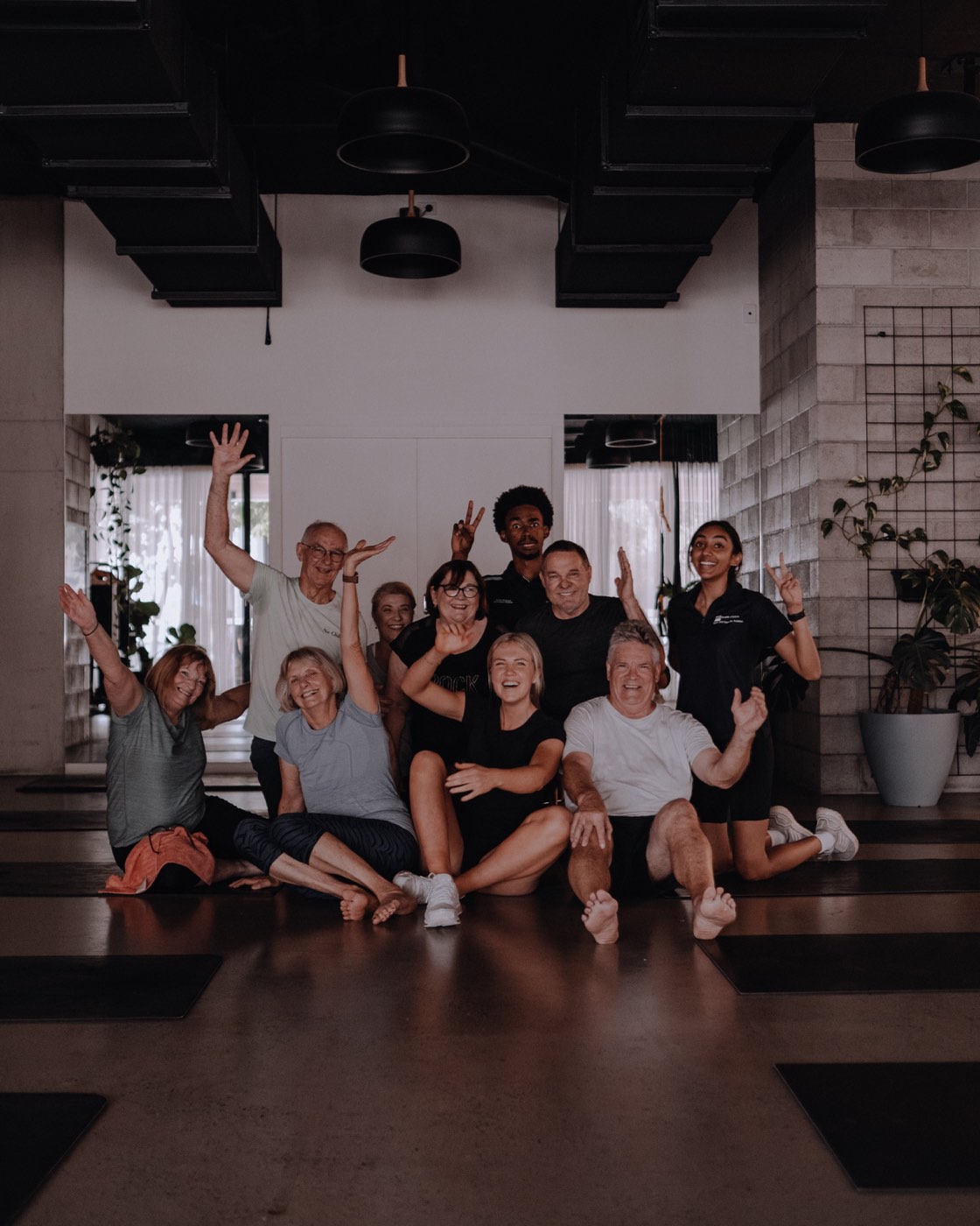 A group of Science of Fitness members in their fifties and sixties sitting together on the studio floor, arms up
